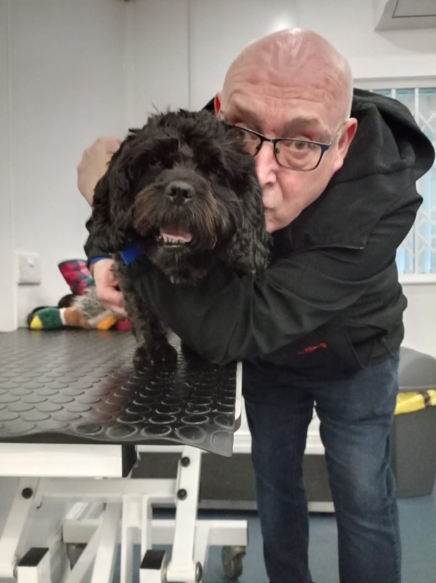 Brian leaning in to cuddle a black cockapoo on a table